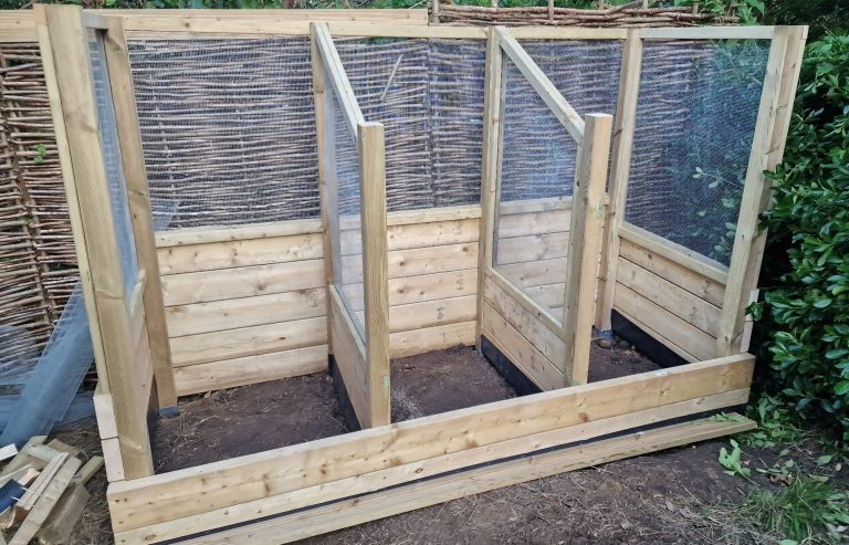 Wooden compost bin structure with three compartments and mesh panels for ventilation.