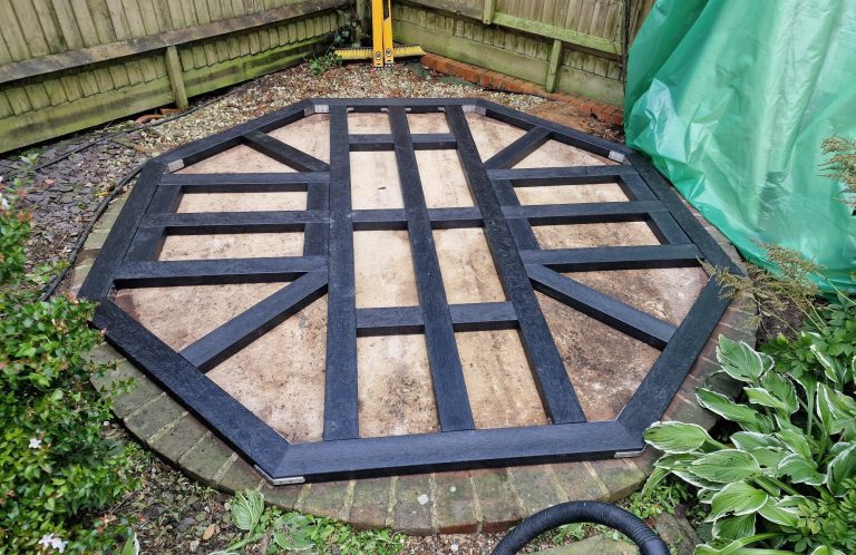 Octagonal composite sub-base frame surrounded by greenery in a garden setting.
