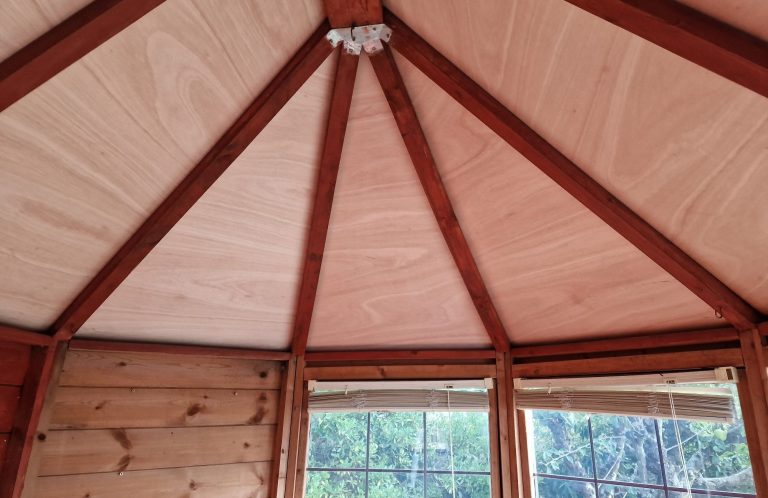 Interior view of a wooden structure with a conical ceiling and large windows.
