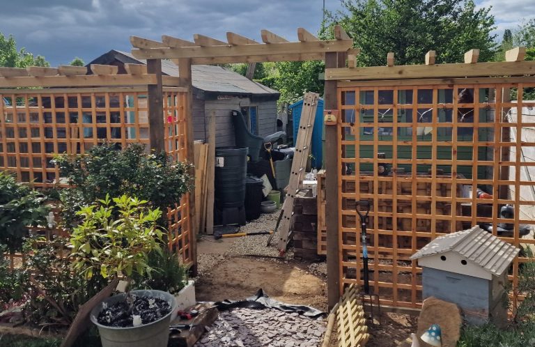 Garden entrance with wooden trellis, potted plants, and a shed in the background.