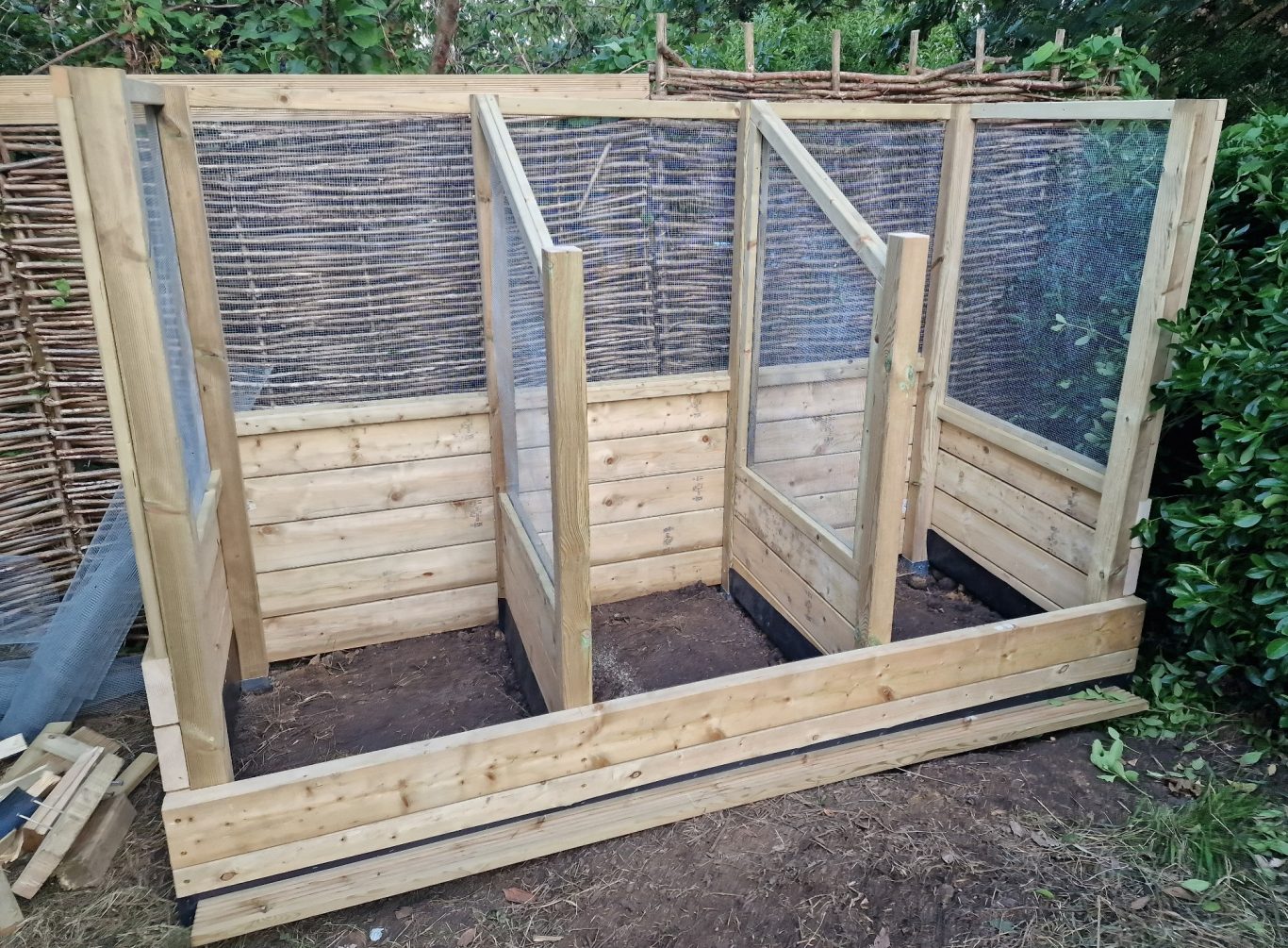 A wooden garden structure with three separate sections and mesh panels.