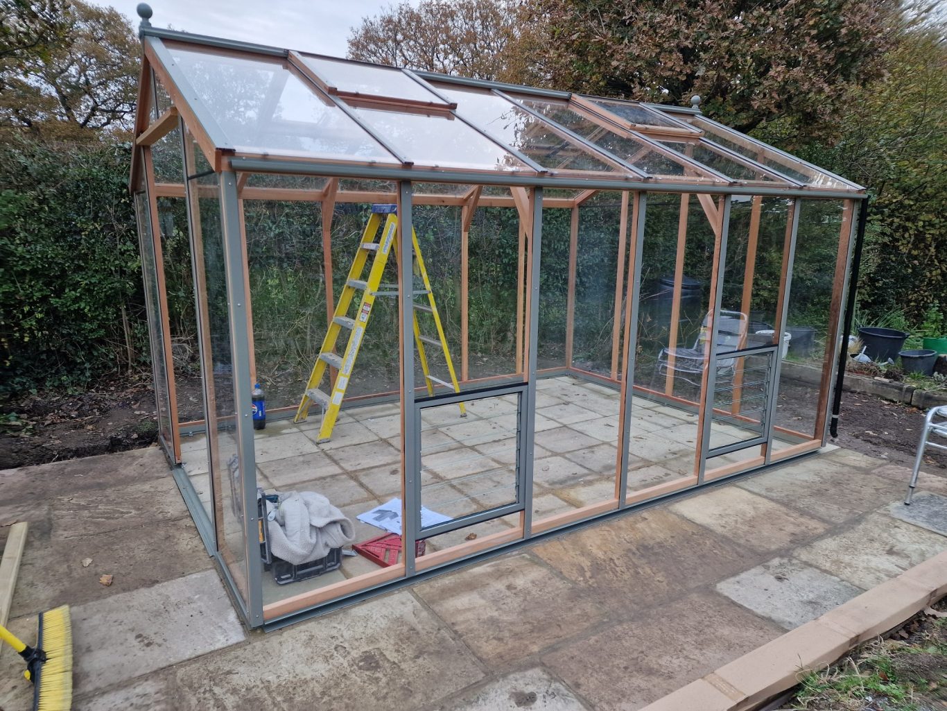 A partially constructed greenhouse with wooden framing and a ladder nearby.