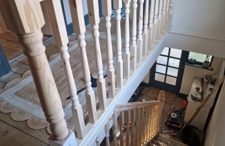 View from above of a staircase with wooden balustrades and a carpeted landing below.