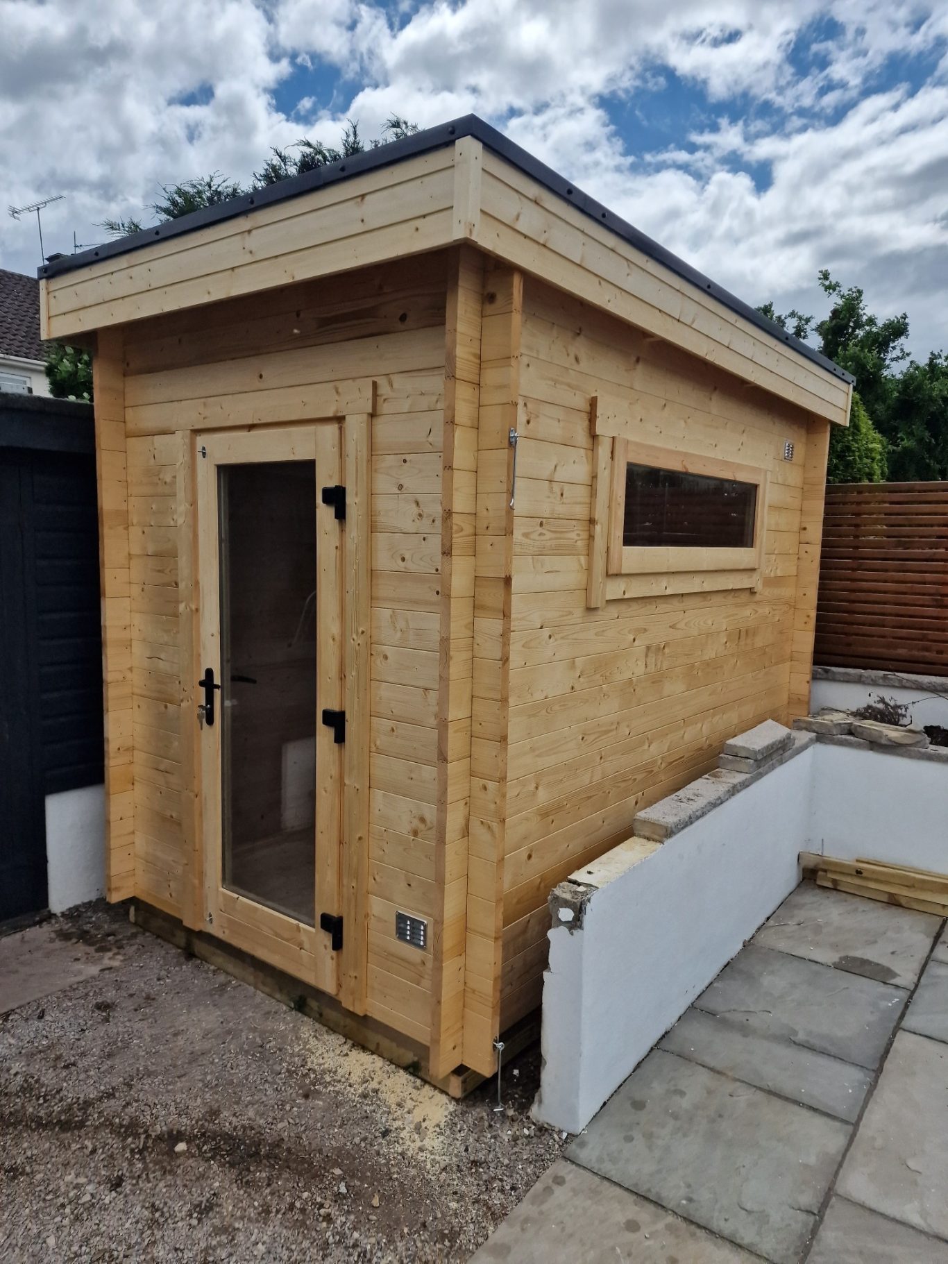 Wooden garden shed with a glass door and small window, set against a cloudy sky.
