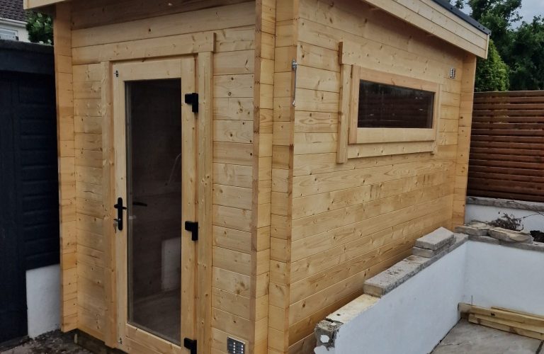 2m x 3m Log Cabin Garden Room with a door and a window, situated in a customers garden.