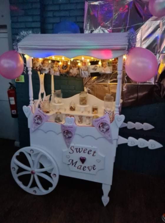 A decorative sweet cart with lights, pink balloons, and a sign reading "Sweet Treats."