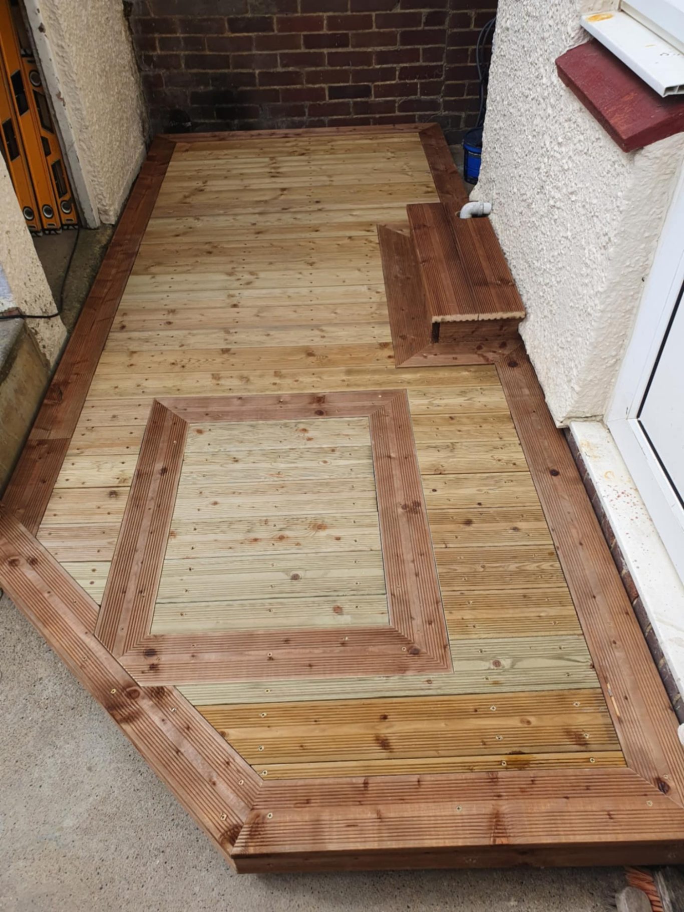 Wooden decked entrance with a rectangular cut-out section and a small wooden plank.